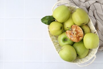 Spoiled apple and good ones in basket on white table, top view. Space for text