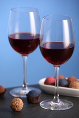 Delicious truffle bonbons and wine on black table against blue background