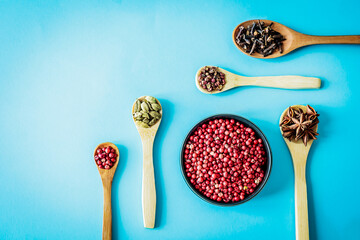 Wide flat-lay of wooden spoons filled with pink pepper, cardamom, cloves, star anise and Sichuan...