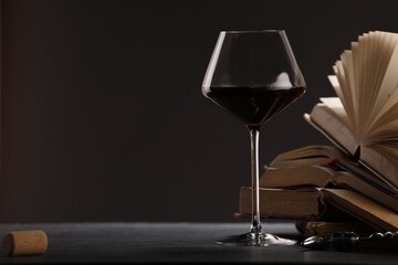 Red wine in glass and books on grey textured table against dark background, closeup. Space for text