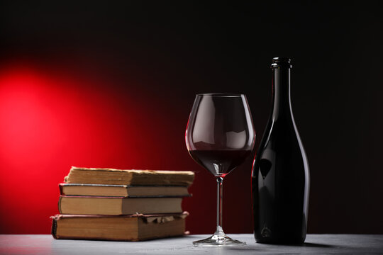 Tasty wine and stacked books on grey table in red light, closeup