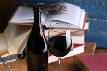 Red wine in glass, bottle and books on wooden table against blue background, closeup