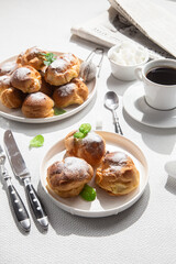Appetizing profiteroles with custard in a white plate on the table. Eclairs, coffee, dessert.