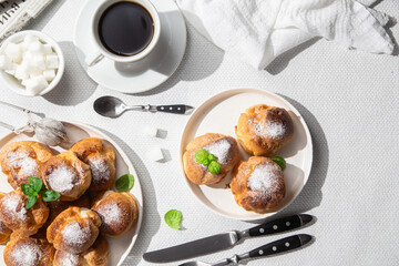 Appetizing profiteroles with custard in a white plate on the table. Eclairs, coffee, dessert.