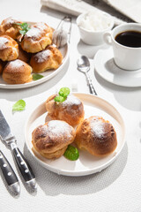 Appetizing profiteroles with custard in a white plate on the table. Eclairs, coffee, dessert.