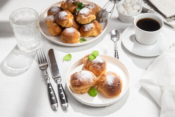 Appetizing profiteroles with custard in a white plate on the table. Eclairs, coffee, dessert.