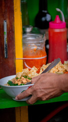 Indonesian chicken noodle (Mie Ayam) dish served at street food stall. The bowl contains noodles,...
