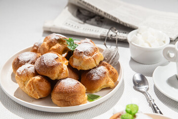 Appetizing profiteroles with custard in a white plate on the table. Eclairs, coffee, dessert.