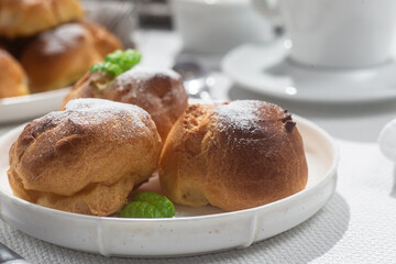 Appetizing profiteroles with custard in a white plate on the table. Eclairs, coffee, dessert.