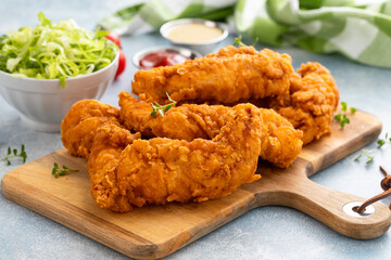 Chicken tenders served on a wooden board with salad and sauces