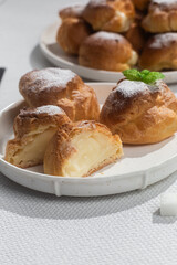 Appetizing profiteroles with custard in a white plate on the table. Eclairs, coffee, dessert.