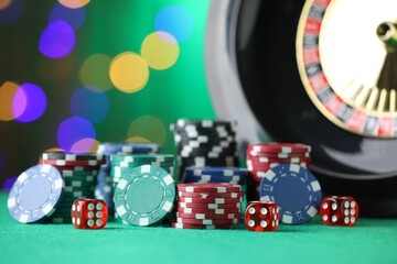 Casino chips, dice and roulette wheel on green table against blurred lights, closeup
