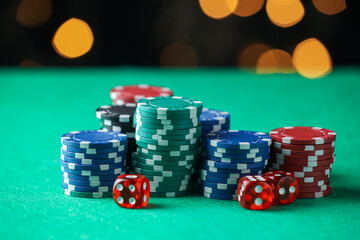 Casino chips and dice on green table against blurred lights, closeup