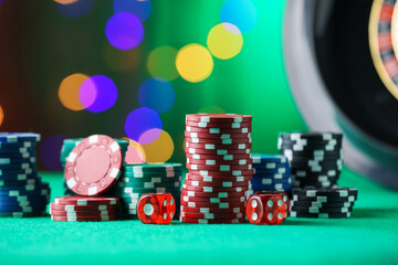 Casino chips and dice on green table against blurred lights, closeup
