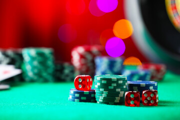 Casino chips and dice on green table against blurred lights, closeup