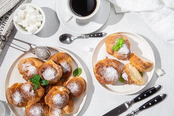Appetizing profiteroles with custard in a white plate on the table. Eclairs, coffee, dessert.