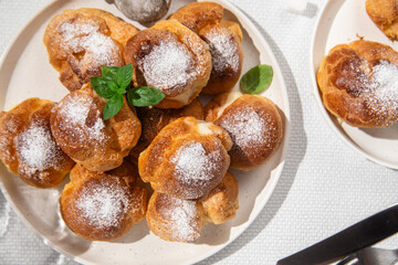 Appetizing profiteroles with custard in a white plate on the table. Eclairs, coffee, dessert.