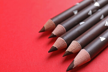 Many eyebrow pencils on red background, closeup. Space for text