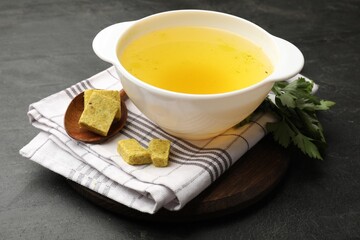 Aromatic bouillon cubes, broth and parsley on black table, closeup