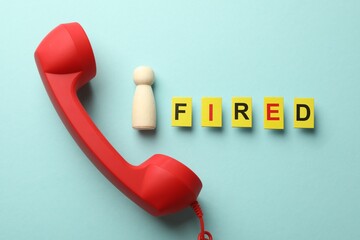 Dismissal. Word fired, telephone handle and human figure on light blue background, flat lay