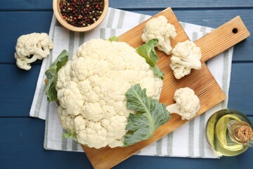 Raw cauliflower, peppercorns and oil on blue wooden table, flat lay