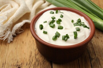 Tasty sour cream in bowl and green onions on wooden table, closeup