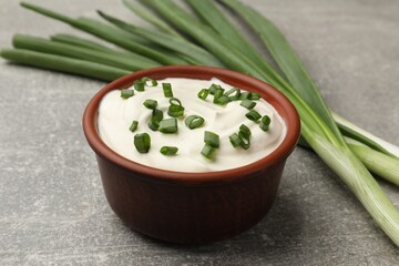 Tasty sour cream in bowl and green onions on grey table, closeup