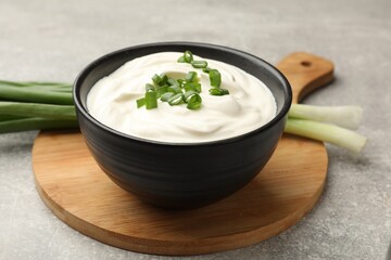 Tasty sour cream in bowl and green onions on grey table, closeup