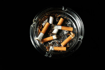 Cigarette butts in ashtray on black background, top view