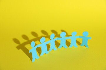 Human paper figures holding hands on yellow background
