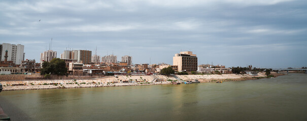 Cityscape of Baghdad along the Tigris River with cloudy skies above the city skyline