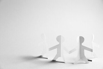 Human paper figures holding hands on light background. Space for text