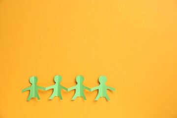 Human paper figures holding hands on orange background, top view. Space for text