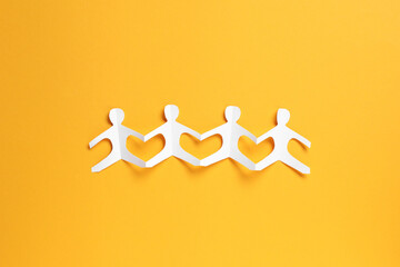 Human paper figures holding hands on orange background, top view