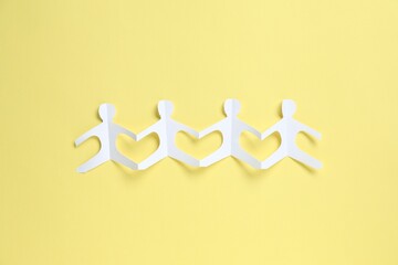 Human paper figures holding hands on yellow background, top view