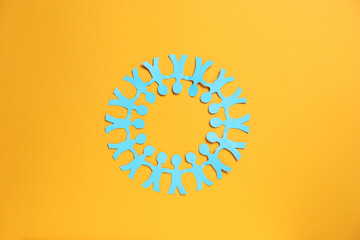 Human paper figures holding hands on orange background, top view