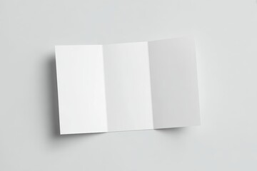 Top-down view of an unfolded white A4 tri-fold brochure laying flat on a smooth light gray surface, all three panels visible, minimalistic and clean design, no text or graphics, soft natural shadows