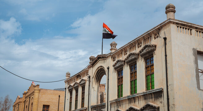 Flag flying over historical building in Baghdad during cloudy day