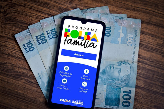 The Bolsa Fam&iacute;lia program is displayed on a smartphone screen with Reais bills in the background. The Brazilian government's Bolsa Fam&iacute;lia program helps the poorest people. 
