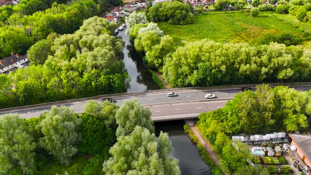 Aerial view of vehicles traversing the A3 highway bridge amidst lush greenery and waterways, creating a vibrant contrast of nature and infrastructure, Guildford, England, United Kingdom.