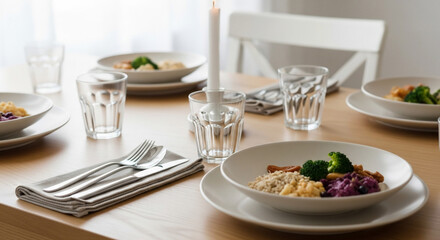 A dining table is set with plates of food, glasses, silverware, and a lit candle, creating a warm and inviting atmosphere for a meal.