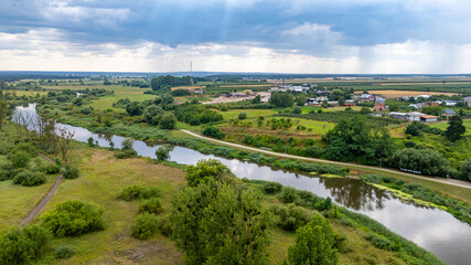 Naklejka premium Aerial view of the town of Pyzdry in Greater Poland and the meandering Warta River. Green fields, riverside buildings, and a small marina create a picturesque rural landscape