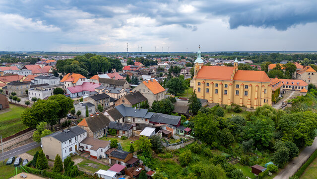 Aerial view of the Baroque church and monastery in Pyzdry. Historic architecture with red roofs surrounded by greenery, with a panoramic view of the town in the background.