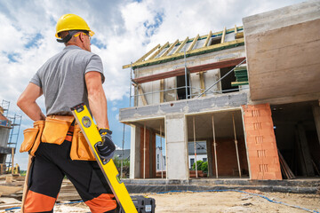 Construction Worker Examines Building Progress With Level in Hand During Daylight
