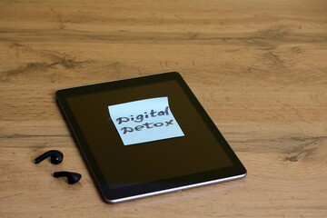 Digital detox reminder note resting on tablet screen with wireless earbuds nearby
