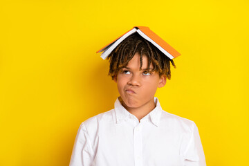 Young Student with a Thoughtful Expression and Book on Head Against a Bright Yellow Background