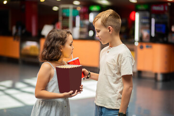 Little girl and teenager kid boy siblings with popcorn and drinks in movie theatre cinema