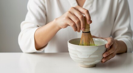 Woman whisking matcha tea in a ceramic bowl with a bamboo whisk for a healthy beverage preparation, with copy space