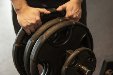 Caucasian young man and bodybuilder picking up heavy dumbbell at gym or fitness center. Close up