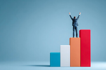 Businessman standing on top of colorful bar chart raising arms celebrating success achievement growth progress leadership concept. Copy space